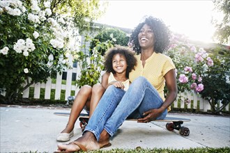 Smiling mother and daughter sitting on skateboard