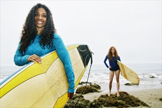 Smiling women holding surfboards at beach