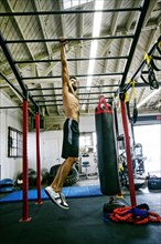 Mixed Race man hanging from bars in gymnasium