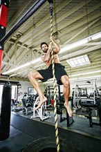Mixed Race man climbing rope in gymnasium