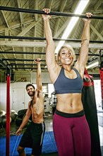 Mixed Race man and woman hanging from bars in gymnasium
