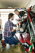 Caucasian father watching son repairing motorcycle in garage
