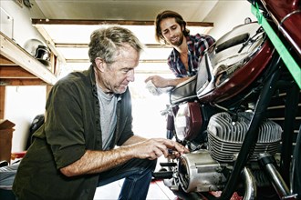 Caucasian son watching father repairing motorcycle in garage