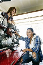 Man watching laughing woman repairing motorcycle in garage