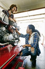 Man watching woman repairing motorcycle in garage