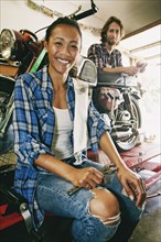 Smiling man and woman repairing motorcycle in garage