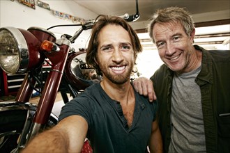 Caucasian father and son posing for selfie with motorcycle in garage