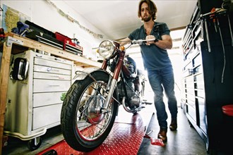 Caucasian man pushing motorcycle on repair stand in garage