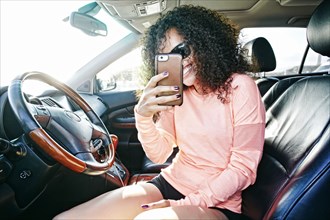 Smiling Hispanic woman in car posing for cell phone selfie