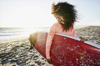Hispanic woman holding surfboard at beach