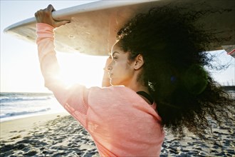 Hispanic woman holding surfboard at beach