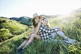 Mother and daughter sitting on hill listening to headphones