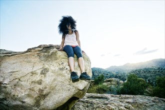 Hispanic woman sitting on boulder in wind