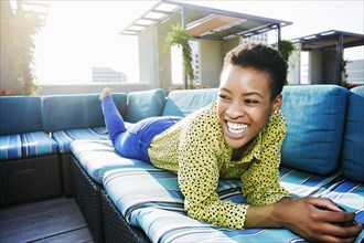 Black woman laying on rooftop sofa laughing