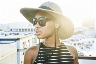 Black woman wearing sun hat and sunglasses on rooftop