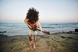 Mixed Race man tossing hair and playing guitar at beach