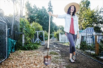 Laughing Caucasian woman leaning on shovel in garden