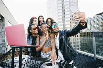 Friends posing for cell phone selfie with DJ on urban rooftop