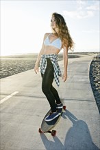 Caucasian woman riding skateboard on path at beach