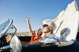 Older Caucasian couple in convertible car with surfboards on beach