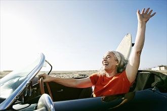 Older Caucasian woman in convertible car with surfboard on beach
