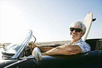 Older Caucasian man in convertible car with surfboard on beach