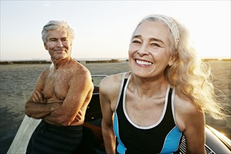 Older Caucasian couple leaning on convertible car at beach