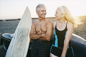 Older Caucasian couple leaning on convertible car with surfboards