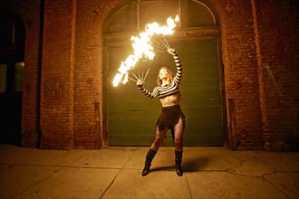 Caucasian woman juggling fire on city sidewalk at night