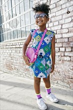 Smiling Black girl standing on sidewalk wearing dress and purse