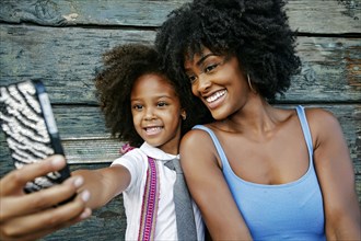 Smiling mother and daughter posing for cell phone selfie