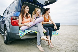 Caucasian women sitting in hatch of car on beach