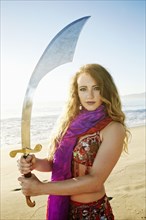 Caucasian belly dancer holding sword on beach