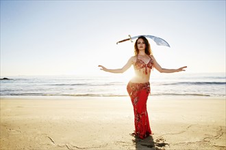 Caucasian belly dancer on beach balancing sword on head