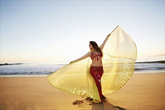 Caucasian belly dancer holding cape on beach