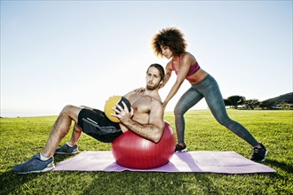 Couple exercising with fitness ball and heavy ball in sunny field