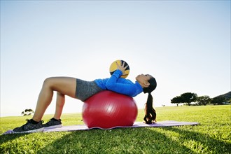 Mixed Race woman exercising with fitness ball and heavy ball in sunny field