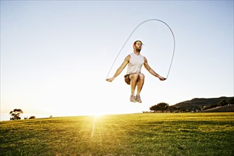Caucasian man jumping rope in sunny field