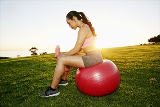 Mixed Race woman resting on fitness ball in sunny field
