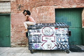 Black woman sitting on dumpster covered with graffiti