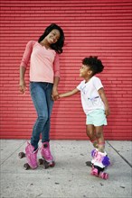 Black mother and daughter wearing roller skates holding hands