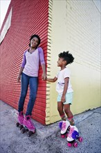Black mother and daughter wearing roller skates holding hands