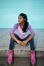 Black woman wearing roller skates sitting on curb