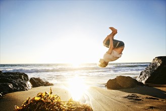 Caucasian man performing backflip on beach