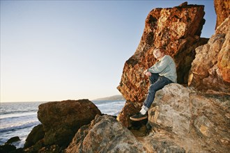 Caucasian man sitting on rock formation at beach
