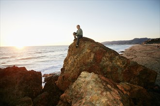 Caucasian man sitting on rock formation near ocean