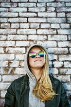 Caucasian woman wearing sunglasses near brick wall
