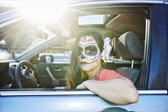 Hispanic woman driving car wearing skull face paint
