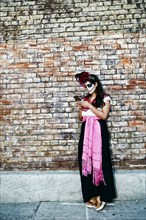 Mixed Race woman on sidewalk wearing skull face paint texting on cell phone