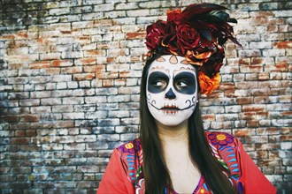 Hispanic woman near brick wall wearing skull face paint